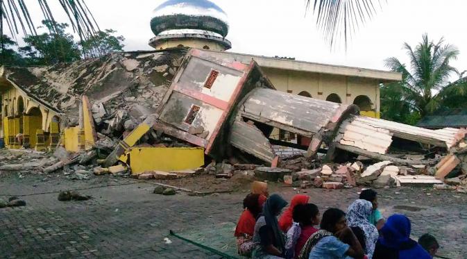 ejumlah warga berkumpul di luar sebuah masjid yang mengalami kerusakan akibat gempa yang mengguncang Kabupaten Pidie Jaya, Aceh, Rabu (7/12). Seperti dirilis BMKG, gempa berkekuatan 6,4 SR mengguncang Aceh sekitar pukul 05.03 WIB. (Zian Muttaqien/AFP)